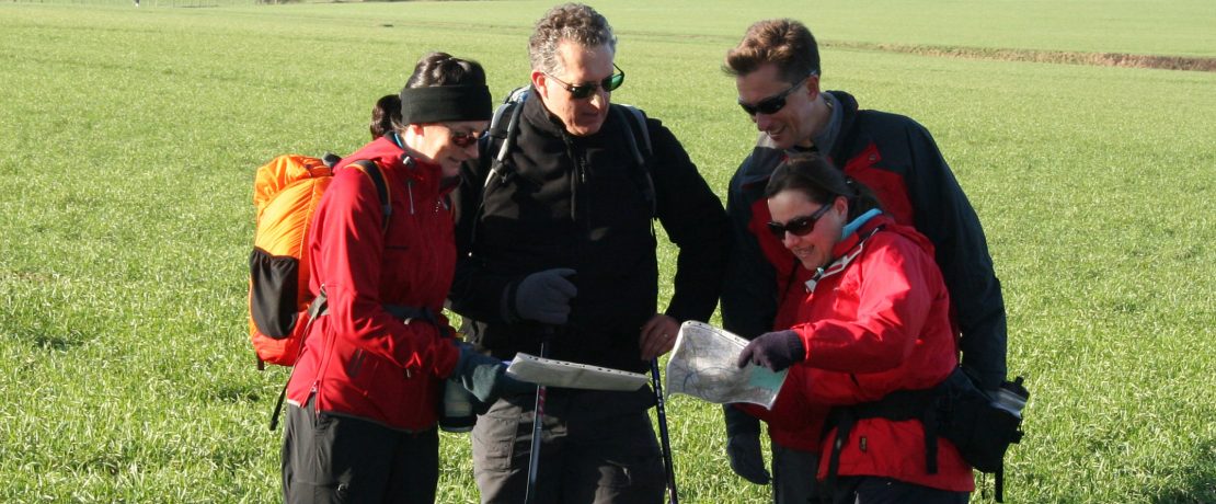 a group of walkers pausing in a green landscape to look at their maps