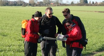 a group of walkers pausing in a green landscape to look at their maps