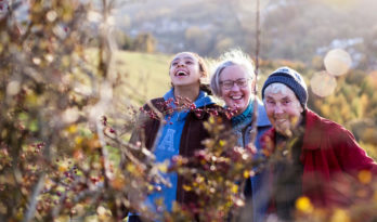 three women from three generations looking at a hedge in the countryside