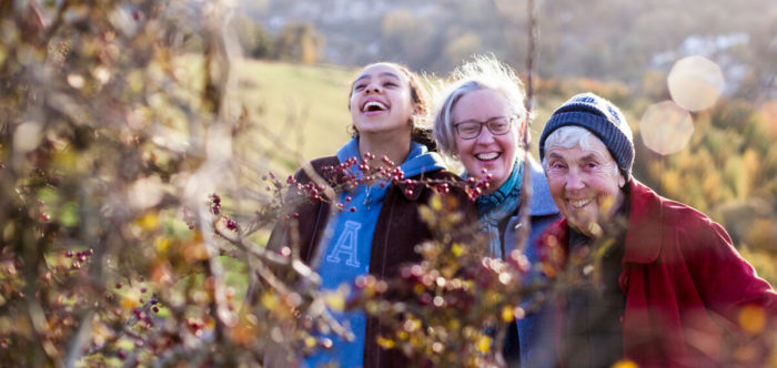 three women from three generations looking at a hedge in the countryside