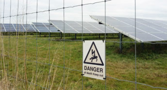 rows of glass photovoltaic panels behind a metal fence with a warning sign that says danger of death keep out