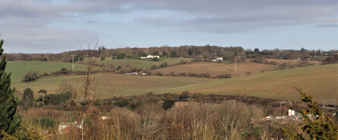 view of the proposed site for an industrial solar farm, showing a wide expanse of undulating hills, open fields, hedgerows