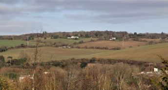 view of the proposed site for an industrial solar farm, showing a wide expanse of undulating hills, open fields, hedgerows