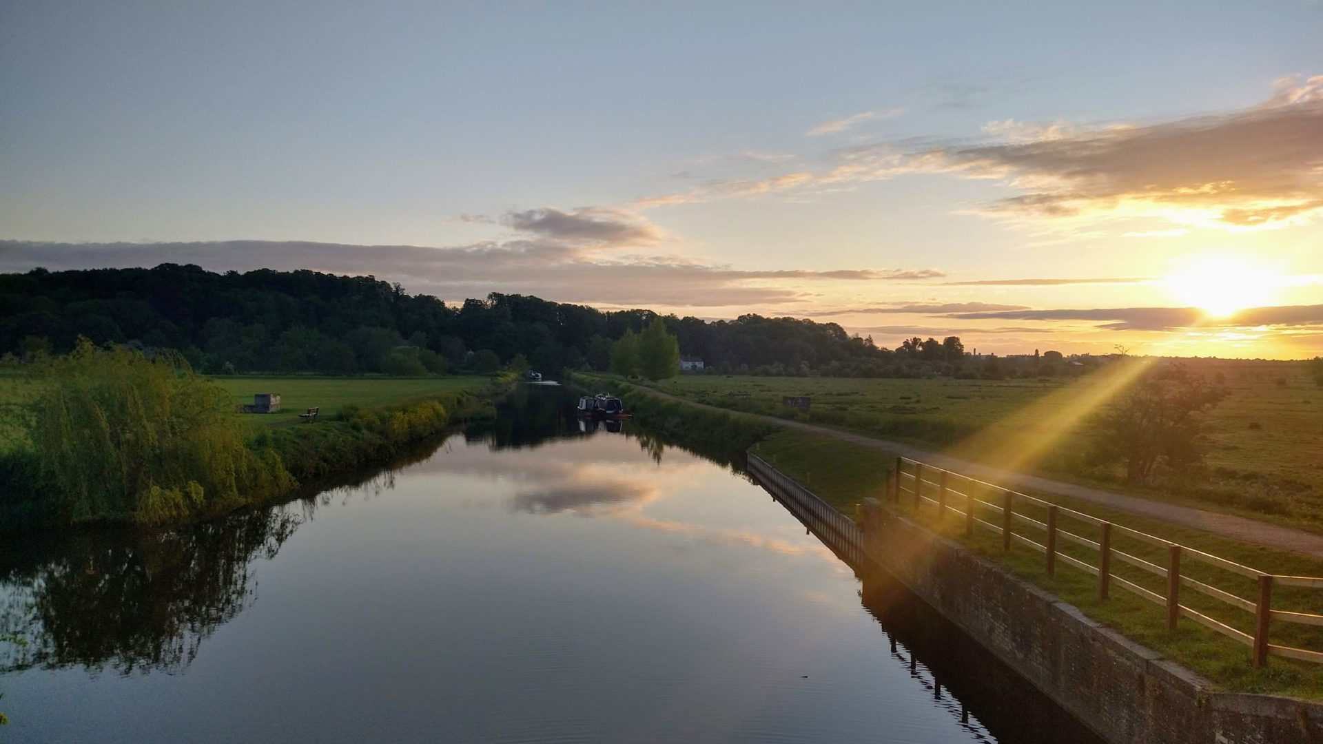 at dawn, the sun rising over green fields and hills, with the river lea in the foreground