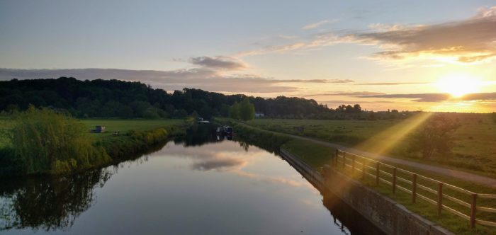 at dawn, the sun rising over green fields and hills, with the river lea in the foreground