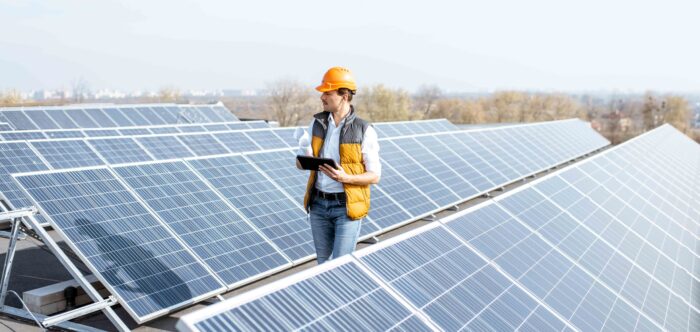 man walking on industrial rooftop and inspecting rows of solar panels