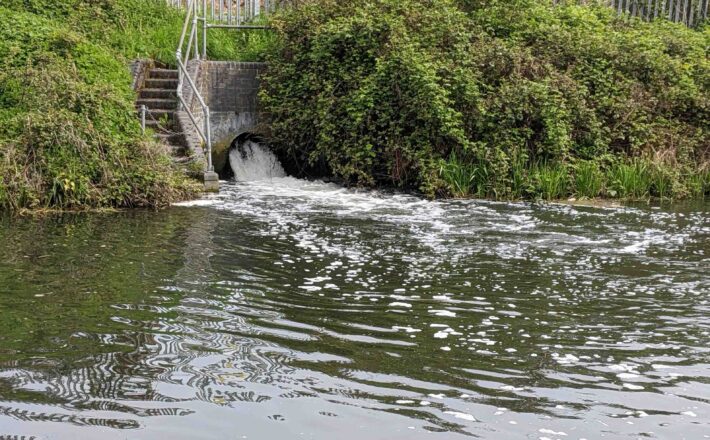 foamy water flowing out of a pipe from sewage treatment works into a canal