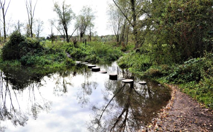 meandering chalk stream with stepping stones across, with lush green riverbanks either side