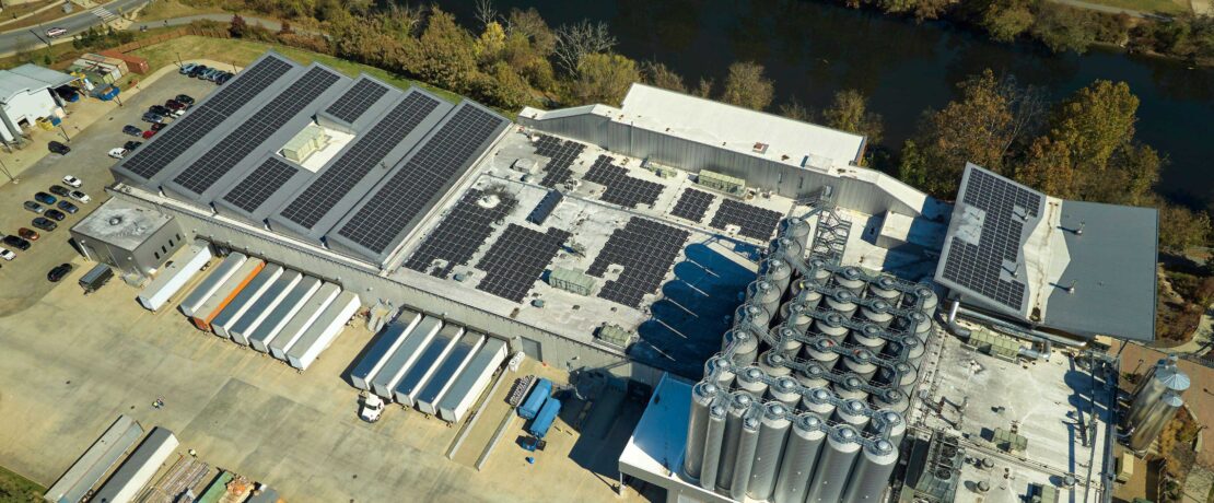 aerial view of blue solar photovoltaic array mounted on rooftop of large industrial building