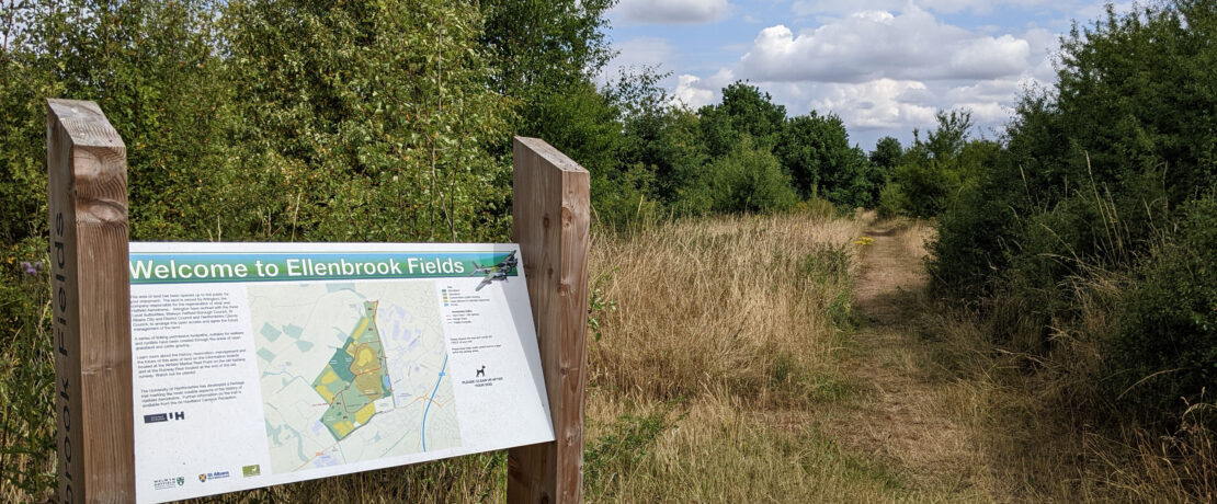 welcome notice at entrance to country park, with grassy path and woodland beyond