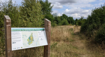 welcome notice at entrance to country park, with grassy path and woodland beyond