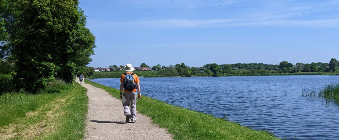 man walking on footpath alongside attractive body of water on a sunny day