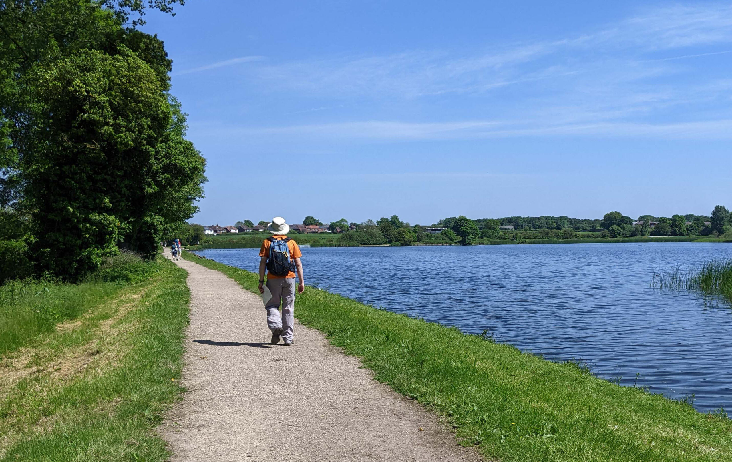 man walking on footpath alongside attractive body of water on a sunny day